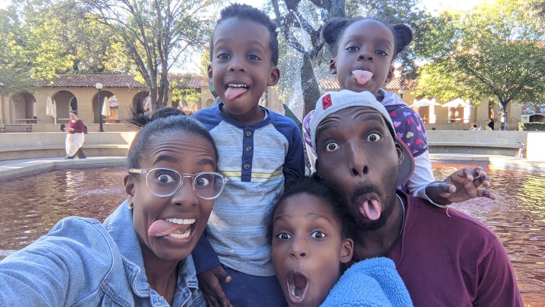 A family making funny faces together in front of a fountain.
