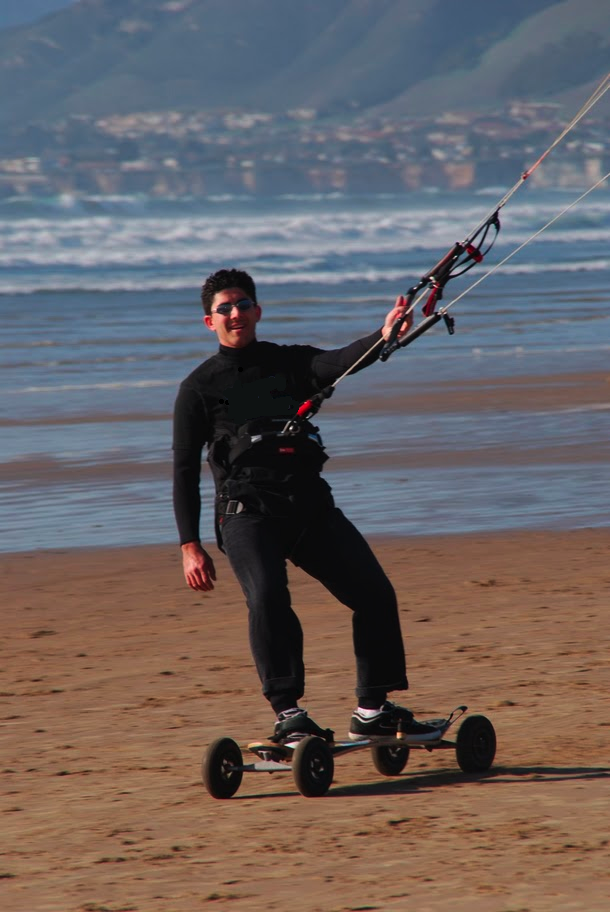 A man riding a skateboard while holding a kite on top of a sandy beach