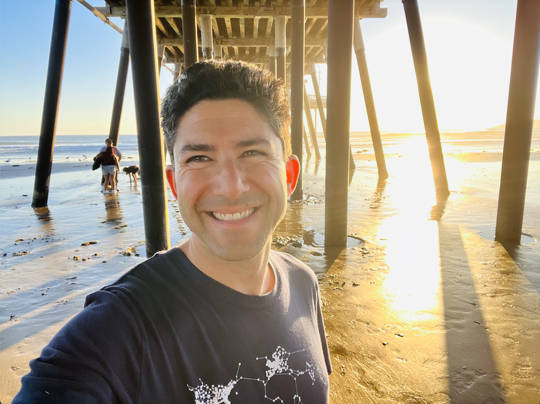 A man standing in front of a pier on the beach
