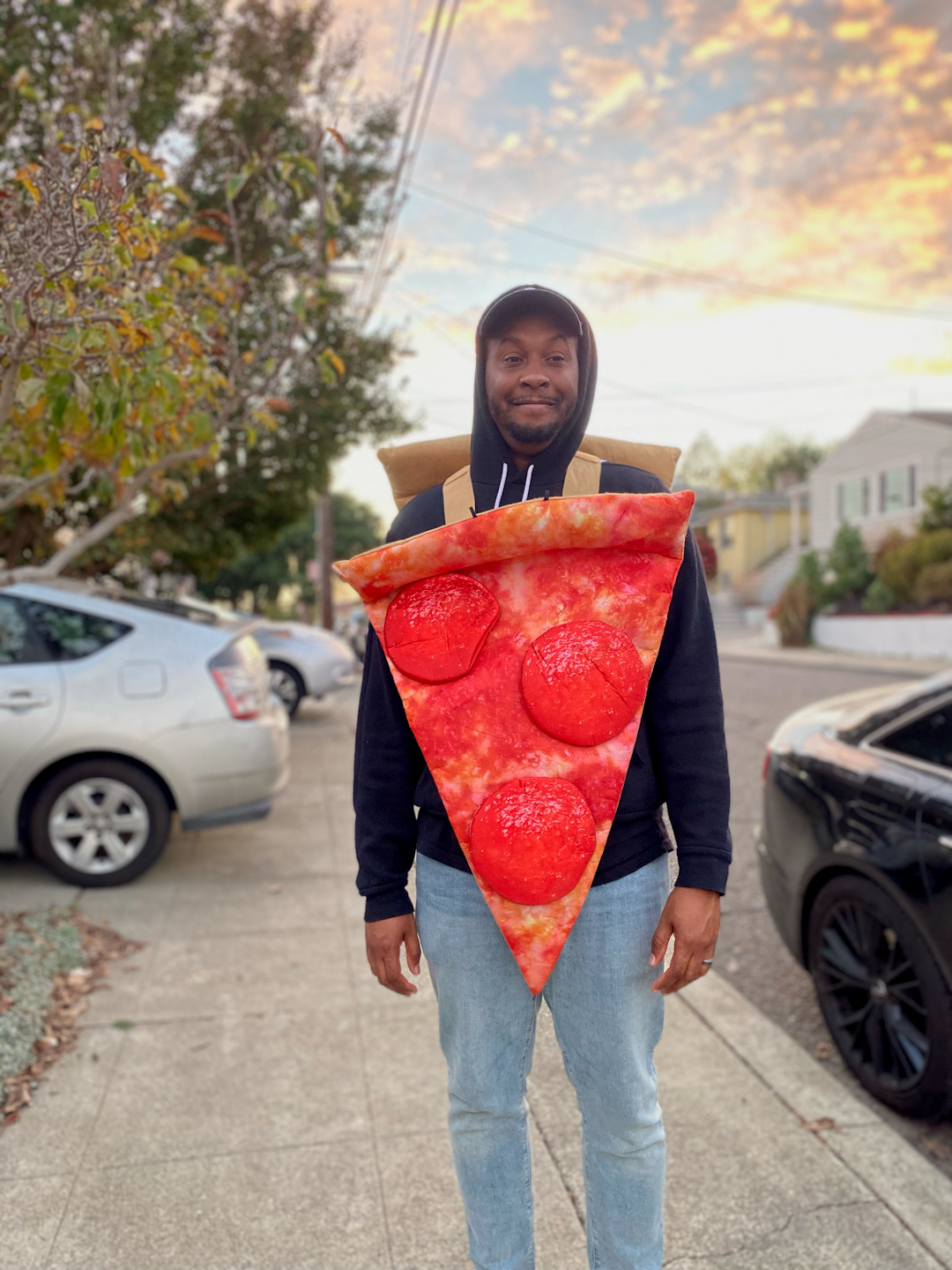 A man standing on a sidewalk wearing a slice of pizza costume